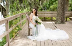 Bride poses with flowers while sitting in a chair on a deck