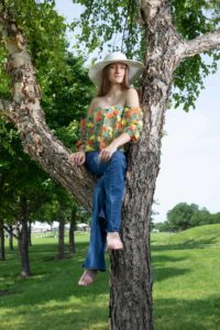Girl wearing hat and jeans sits in a tree