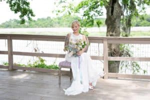 Blonde bride holds bouquet and sits on a deck