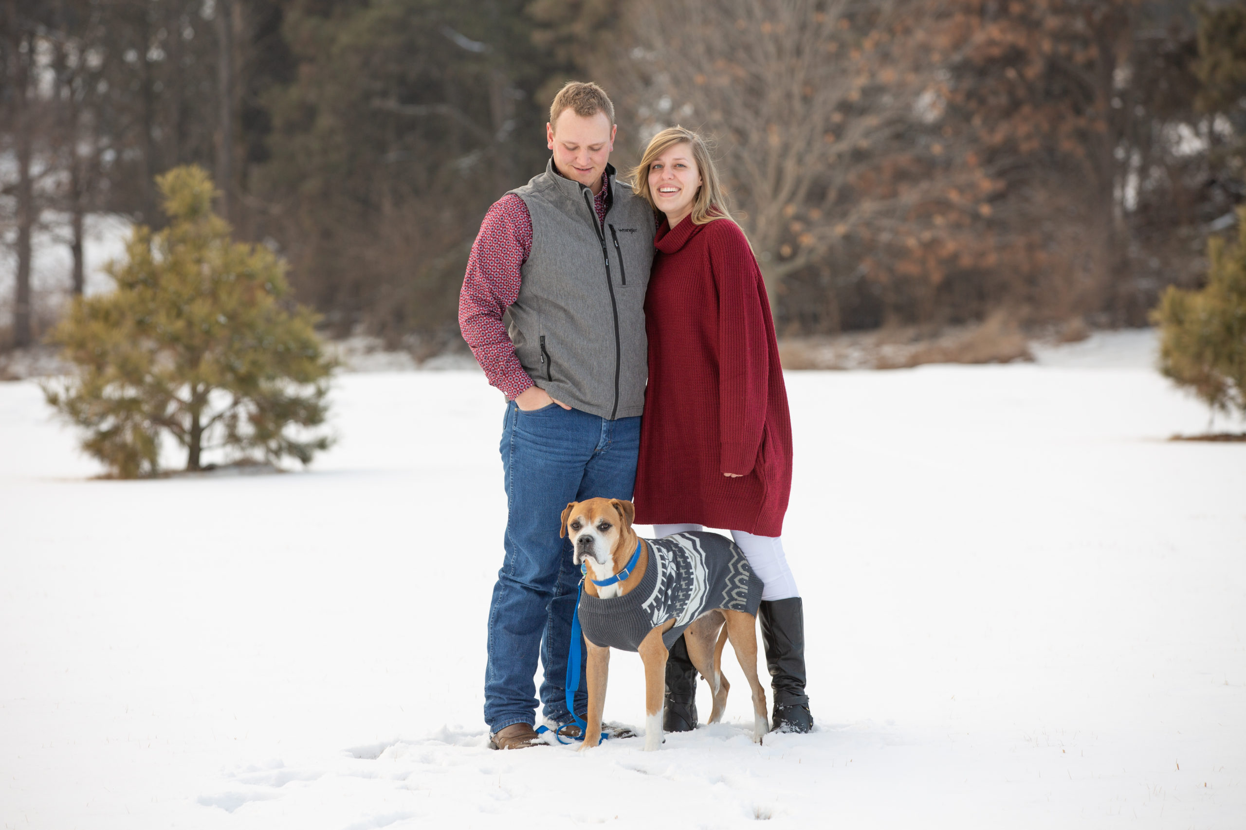 couple poses in the snow with their dog