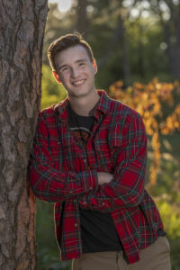 George leans against a tree in his red plaid shirt