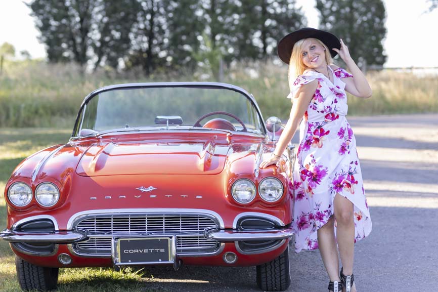girl stands by red car at her senior photo shoot