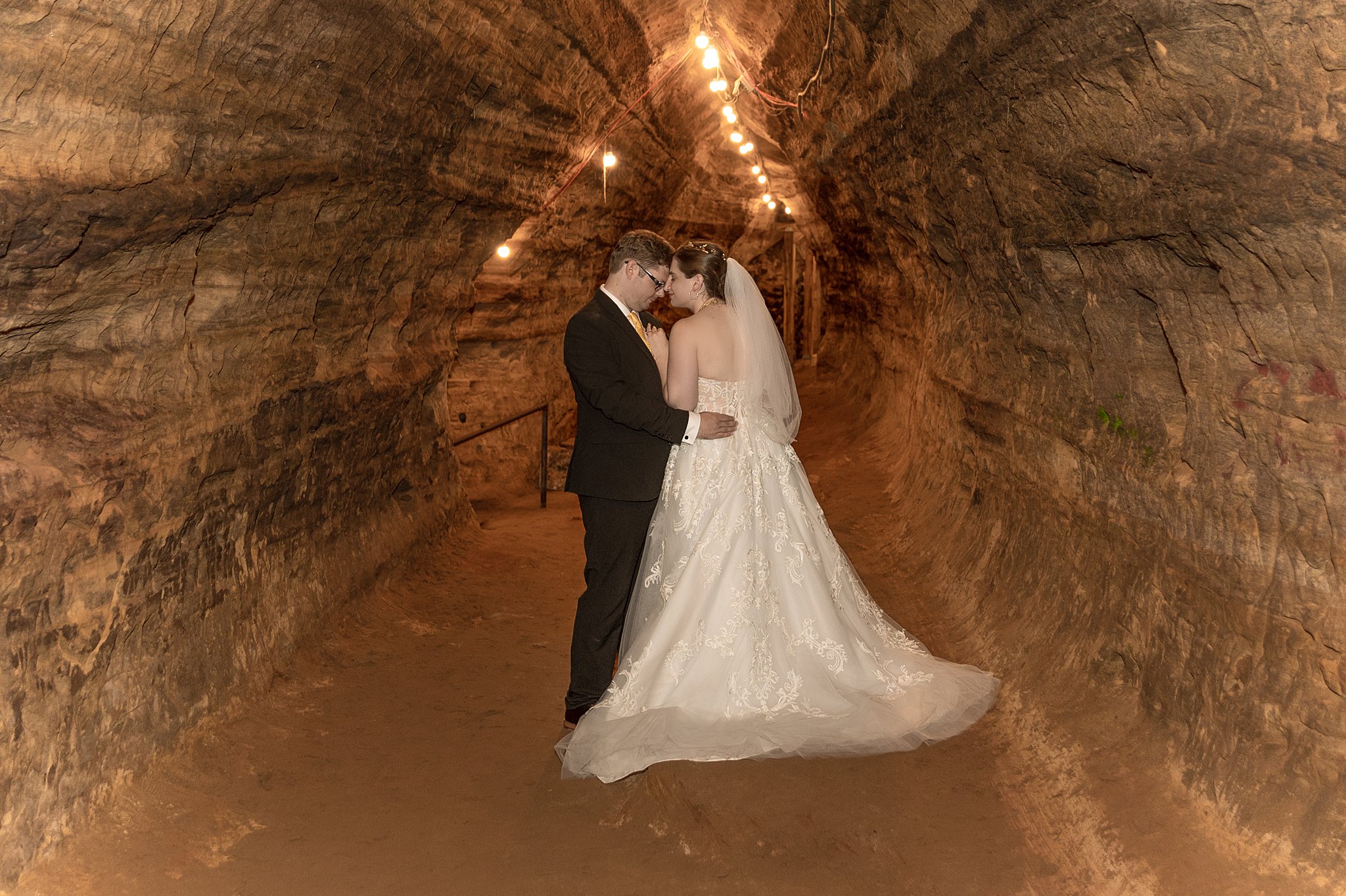newlyweds embrace in the center o a cave with lights robbers cave lincoln ne