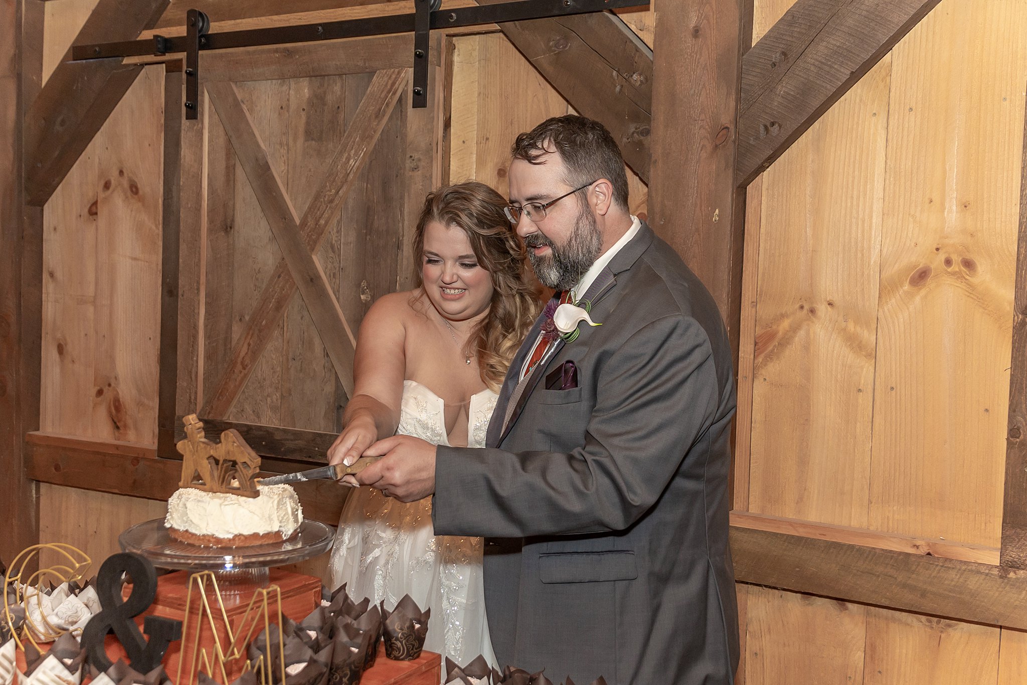 Newlyweds cut the cake in front of barn window