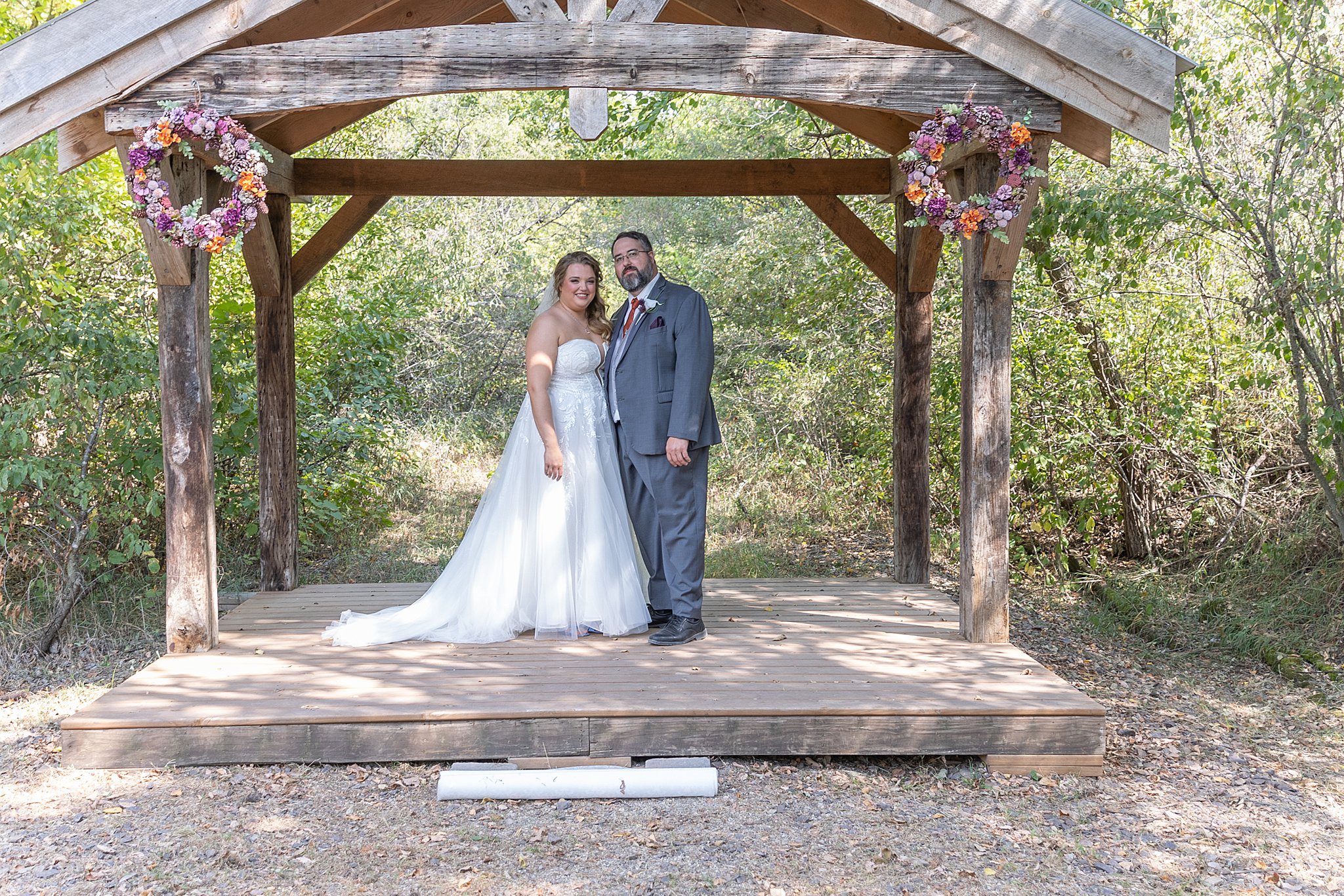 newlyweds stand in a wooden gazebo decorated with colorful wreathes