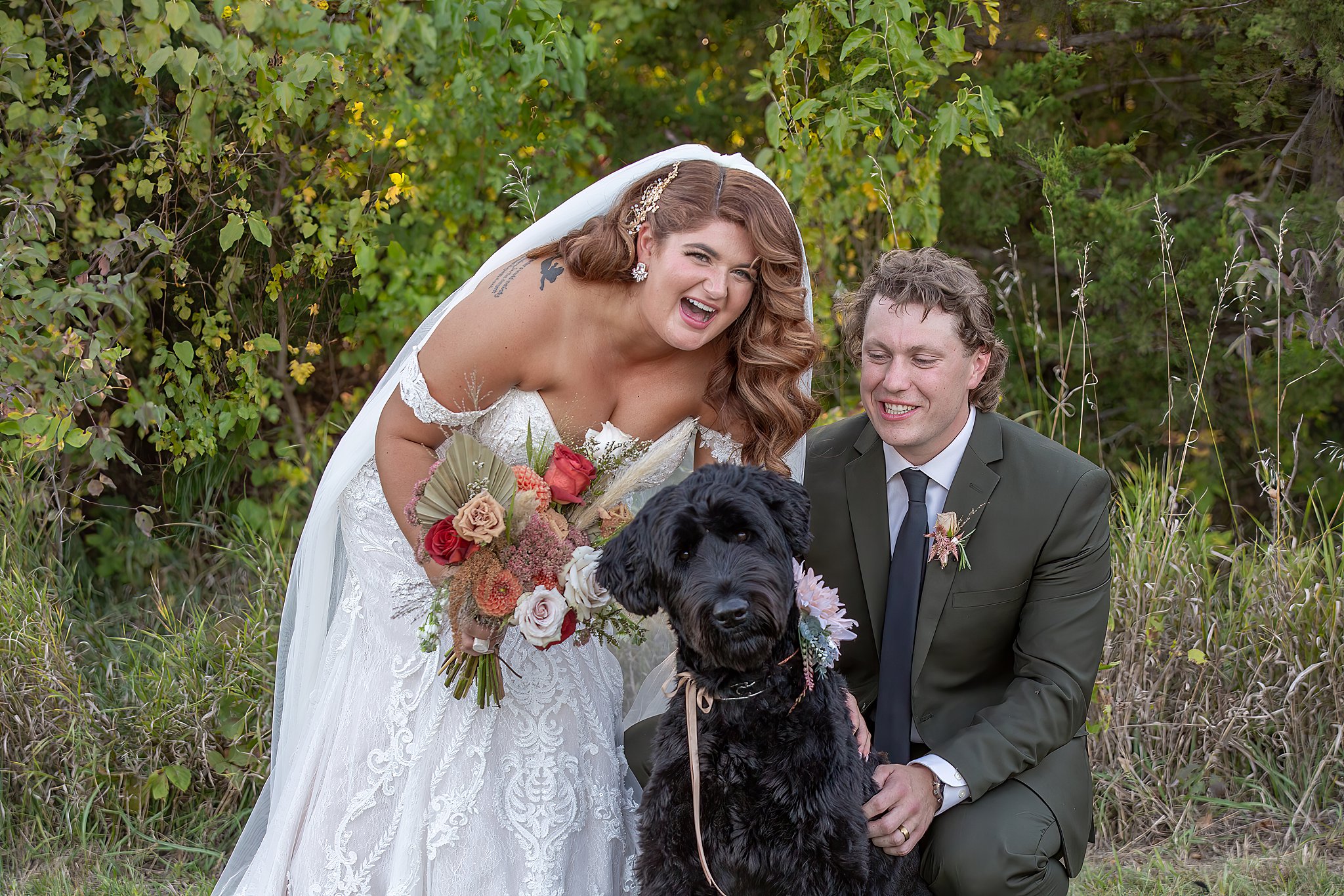 Newlyweds play in a forest with their large black dog