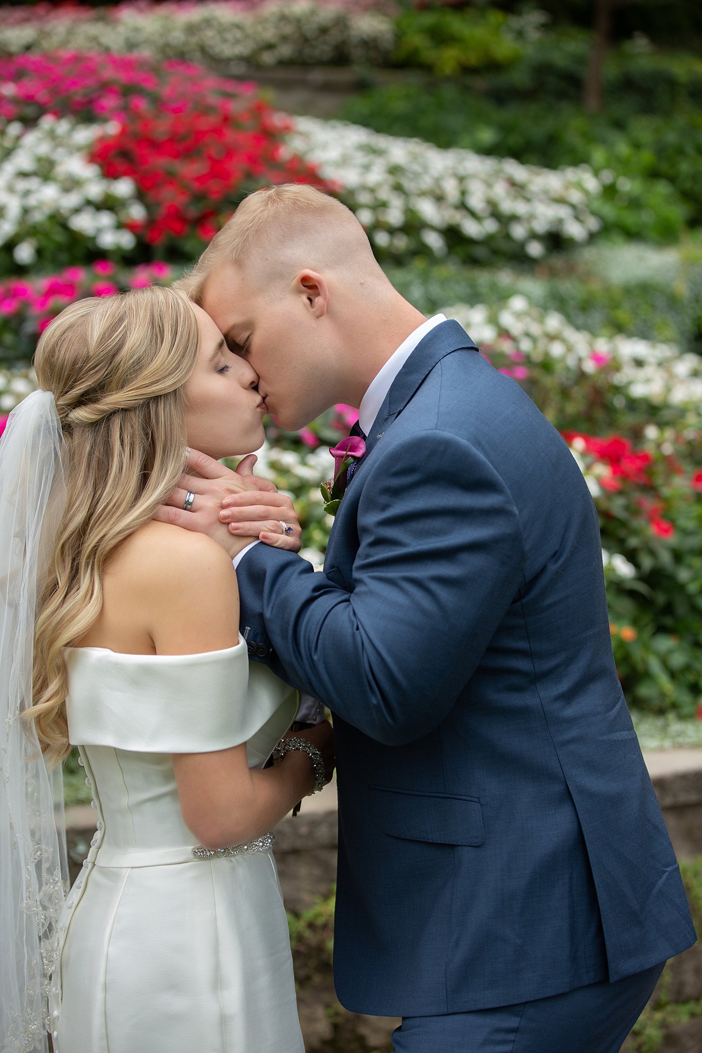 Newlyweds kiss in blooming flower garden with a stone wall