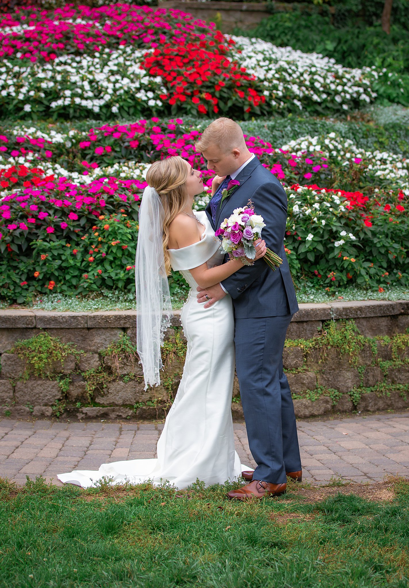 Newlyweds stare in each other's eyes while chest to chest in front of a large display of pink, red and white flowers sunken gardens wedding lincoln ne