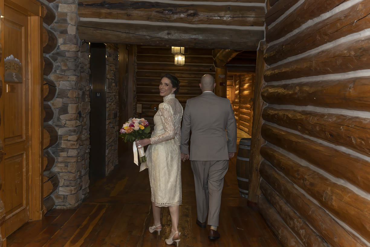 Newlyweds walk down a hall in a log cabin while holding a colorful bouquet Wilderness Ridge wedding