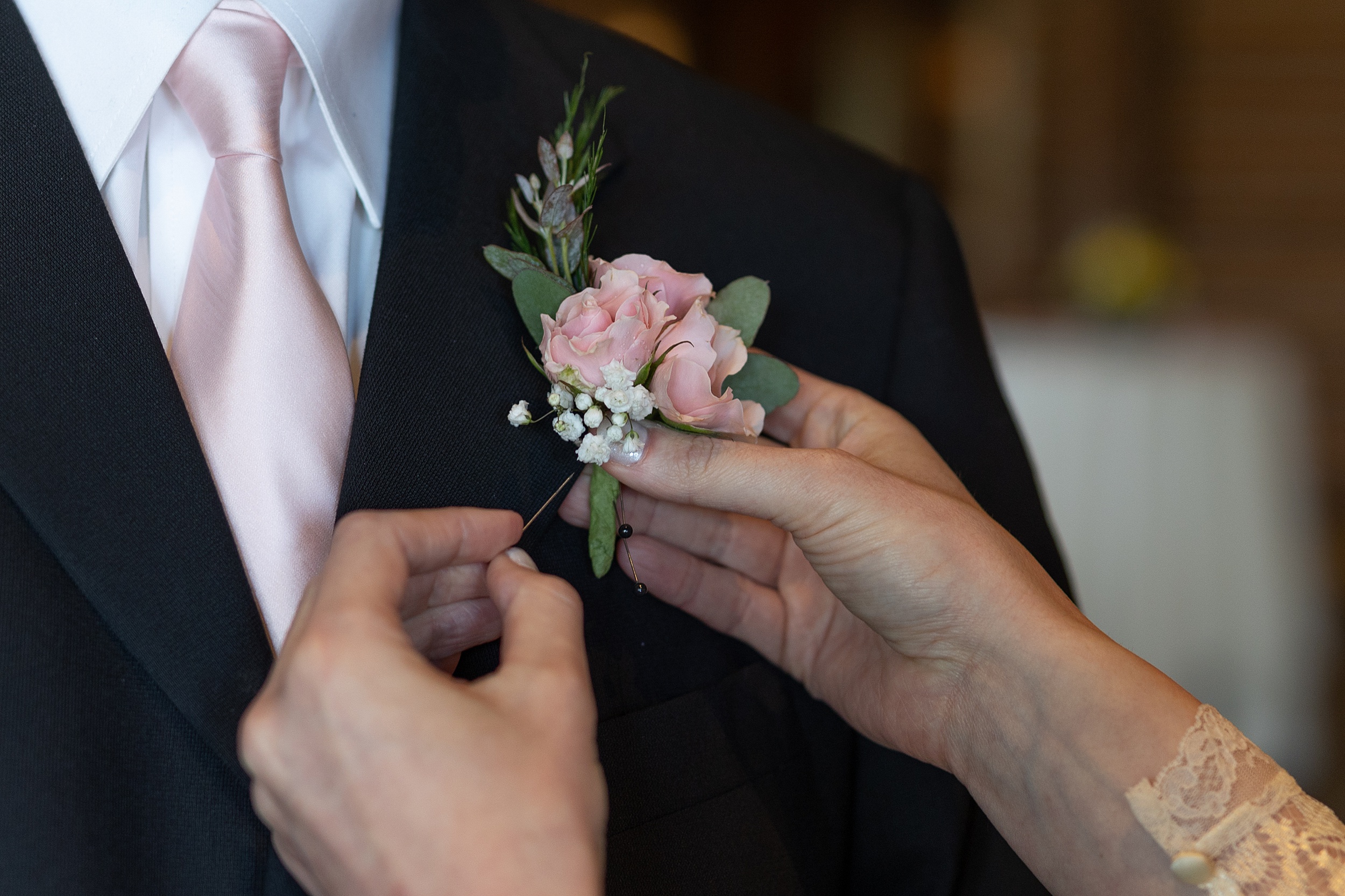 Detail of mother pinning a corsage onto the groom in a pink tie