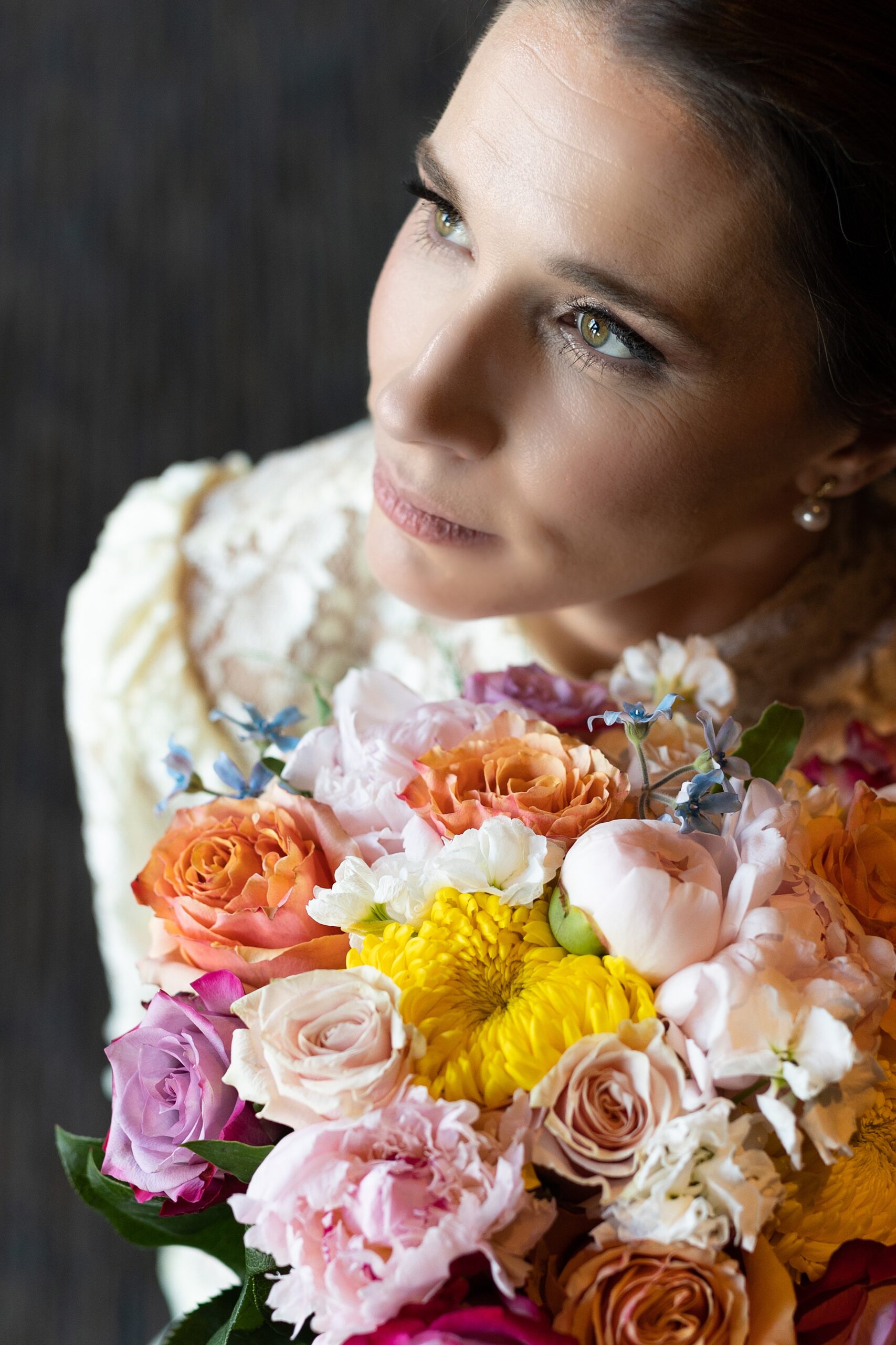 A bride in a vintage lace dress holds her colorful bouquet under her chin in front of a window the diamond room omaha