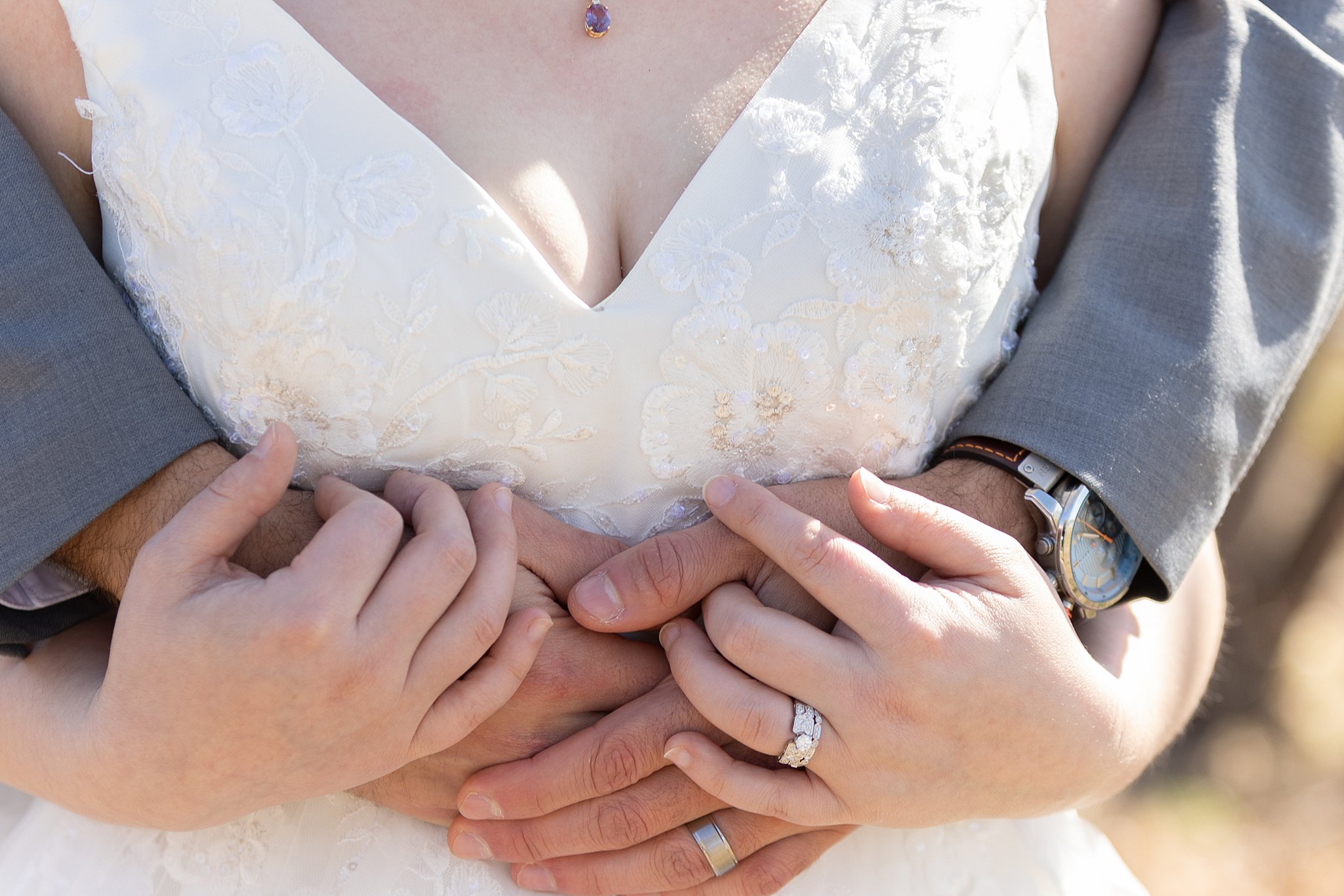 Details of newlyweds hugging with a lace dress and grey suit