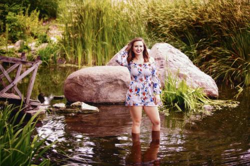 senior girl stands in water in front of rock
