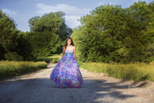 Girl in blue and purple gown walks along a country road