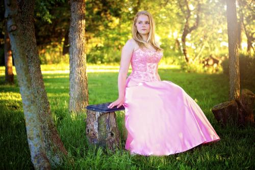 Girl in pink dress sits on a bench surrounded by trees